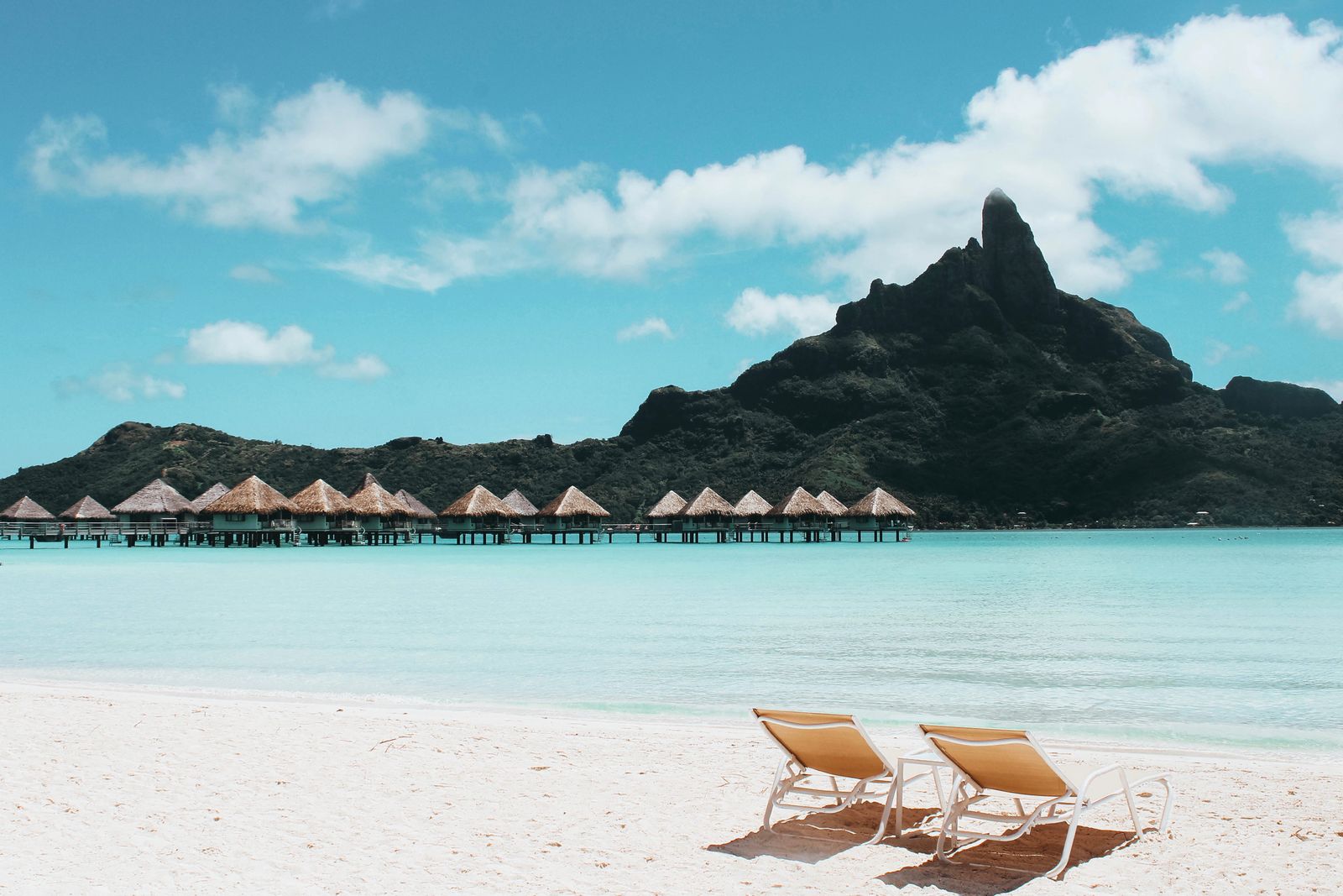 Sun loungers under palm trees beside a calm turquoise lagoon
